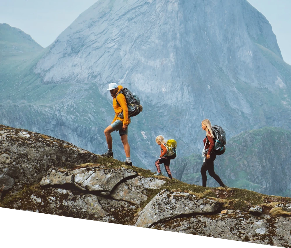 Tres excursionistas con mochilas subiendo por un sendero, con un pico de montaña al fondo.