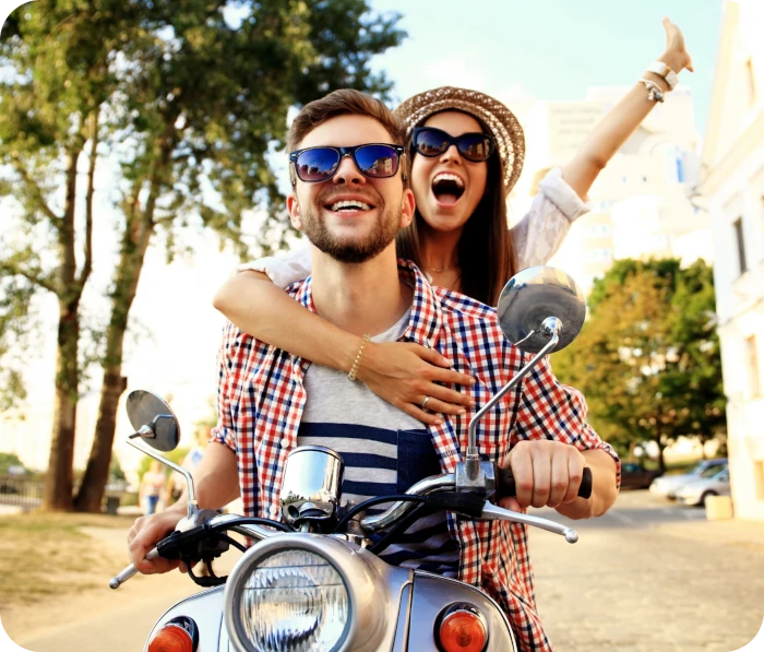 Una pareja sonriendo mientras conducen una motocicleta en un día soleado.